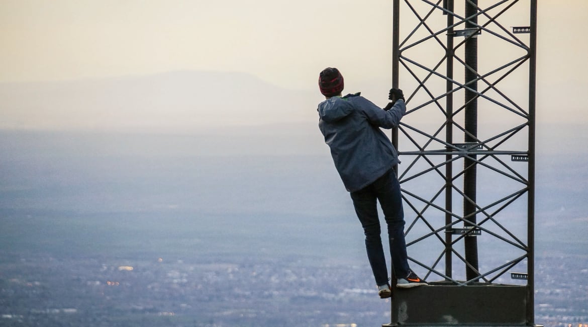 Man on a radio tower looking over a city - by Jack Sloop from Unsplash