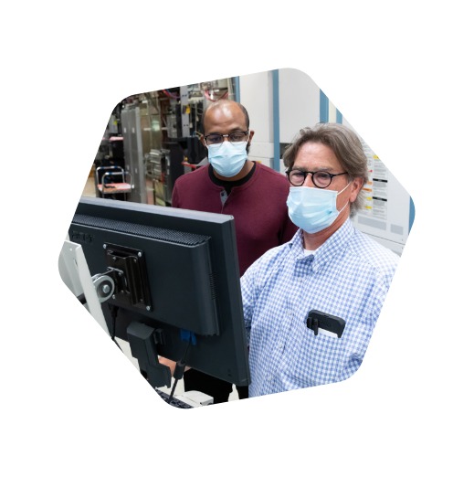 Two men in masks looking at a computer monitor